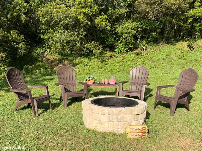 Adirondack chairs surrounding a stone fire pit in the grass