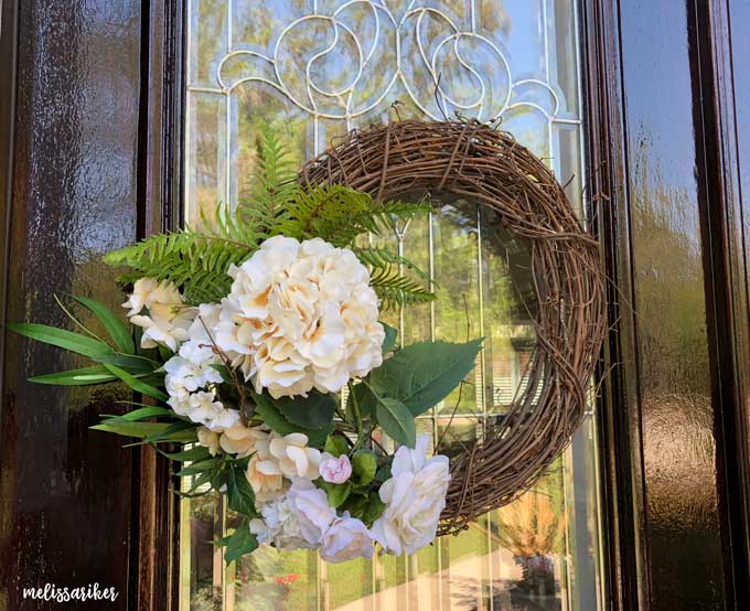 grapevine wreath with faux fern and flowers on wooden door with glass window