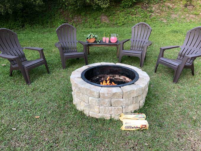 Adirondack chairs near stone fire pit and lemonade pitcher and glasses on table in background