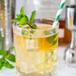 close up of mint julep in a clear glass with mint garnish and green and white striped straw