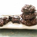 chocolate cookies stacked on white plate with one next to them broken in half