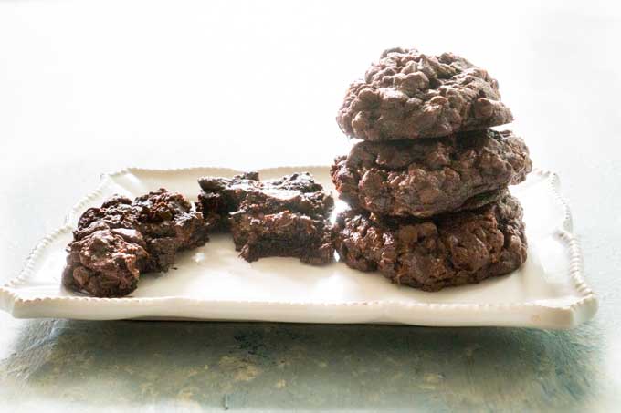 chocolate cookies stacked on white plate with one next to them broken in half