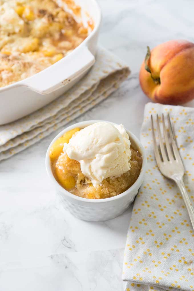 peach cobbler in white ramekin with ice cream