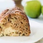 A close up of a piece of apple cake on a plate with green apple in background