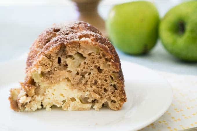 A close up of a piece of apple cake on a plate with green apple in background