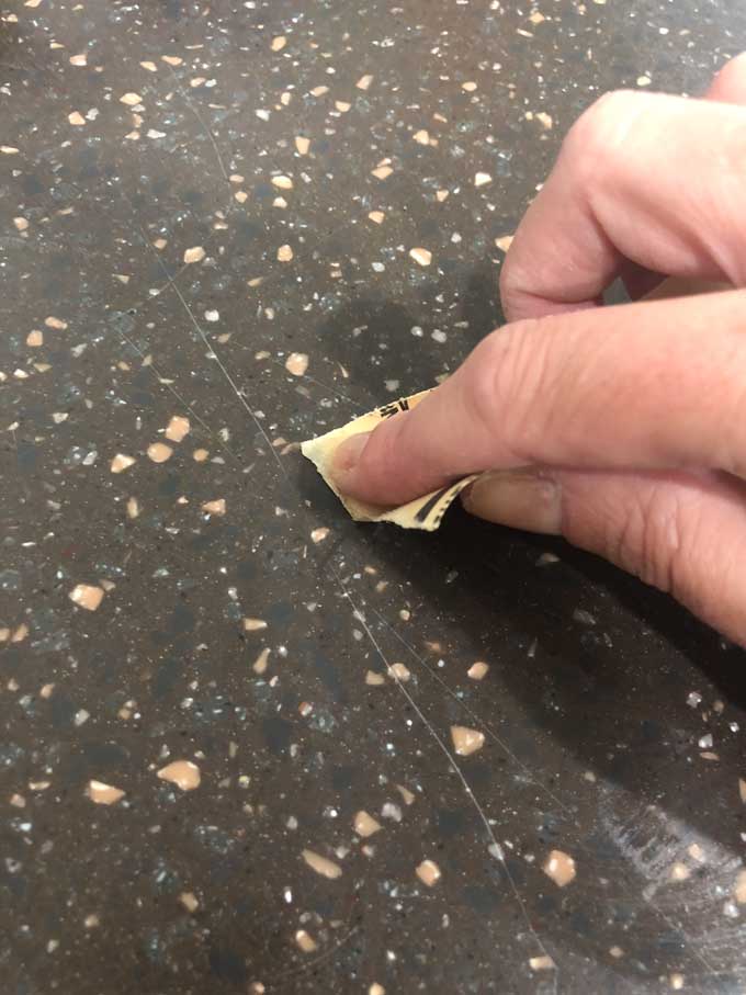 A close up of a hand sanding scratched dark corian countertop