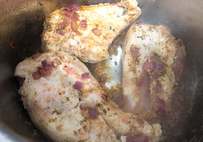 A close up of chicken breasts in pan with broth and diced onions