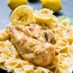 A close up of farfalle pasta with chicken breast on top with lemons in background