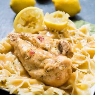 A close up of farfalle pasta with chicken breast on top with lemons in background