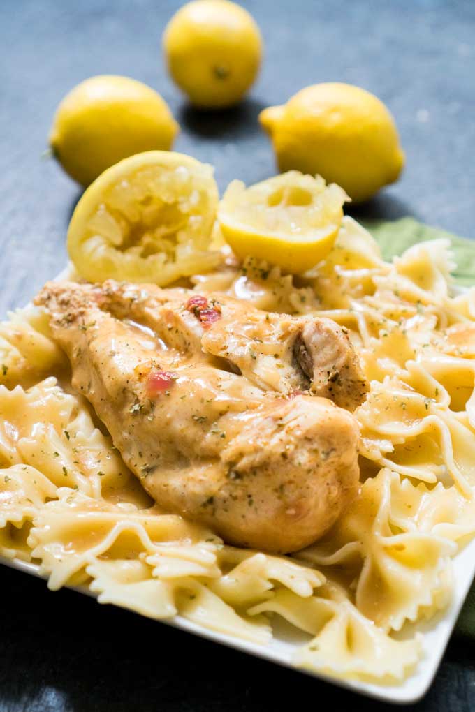 A close up of farfalle pasta with chicken breast on top with lemons in background