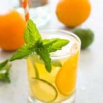 glass of orange mojito with mint garnish and orange and white striped straw