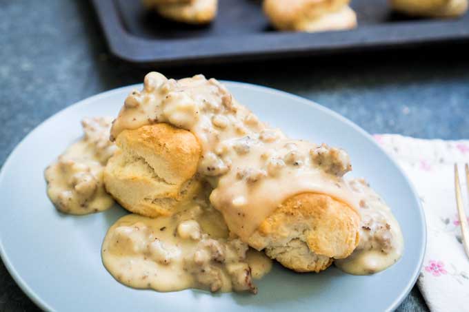 homemade country sausage gravy over biscuits on blue plate