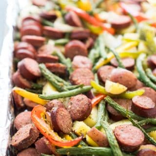 A close up of sausage and veggies on baking sheet