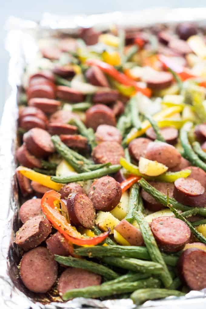 A close up of sausage and veggies on baking sheet