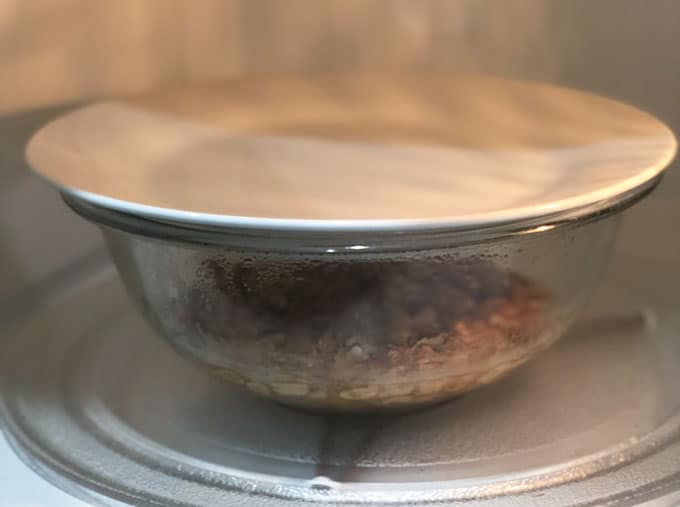 A close up of a bowl in microwave with plate on top