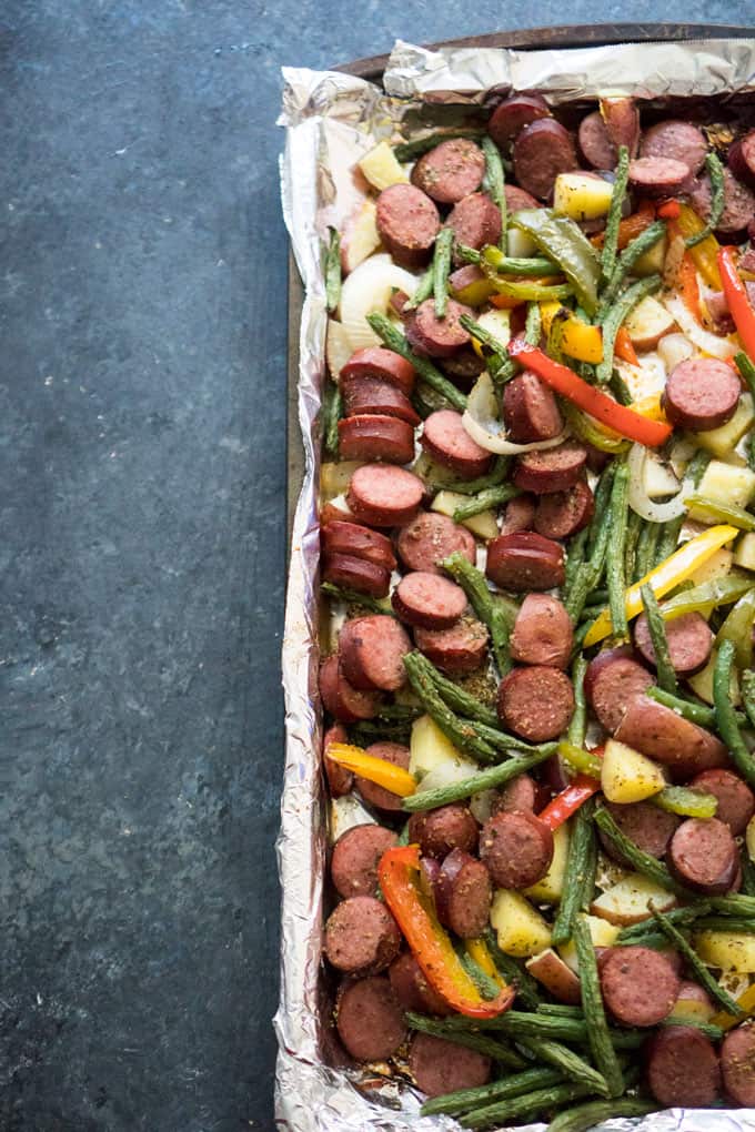 overhead view of sausage and chopped vegetables on foil elined baking dish