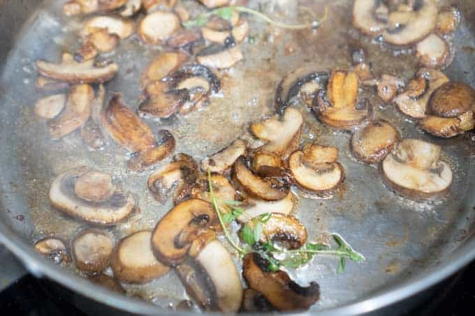 sliced mushrooms sautéing with herbs in metal pan