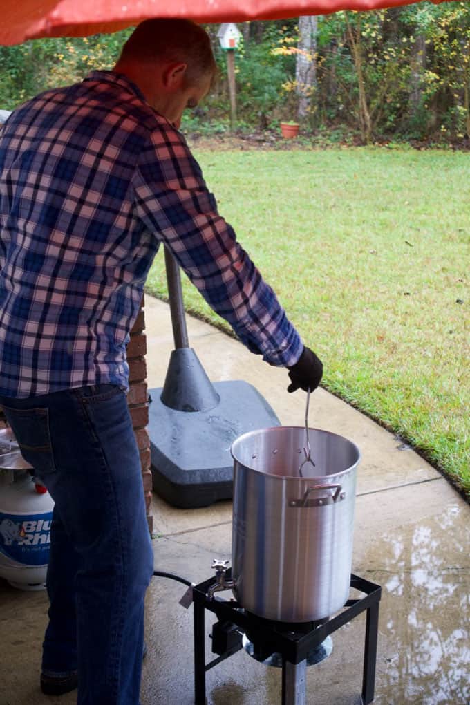 A tall man is cooking a turkey in a turkey fryer with grass in background