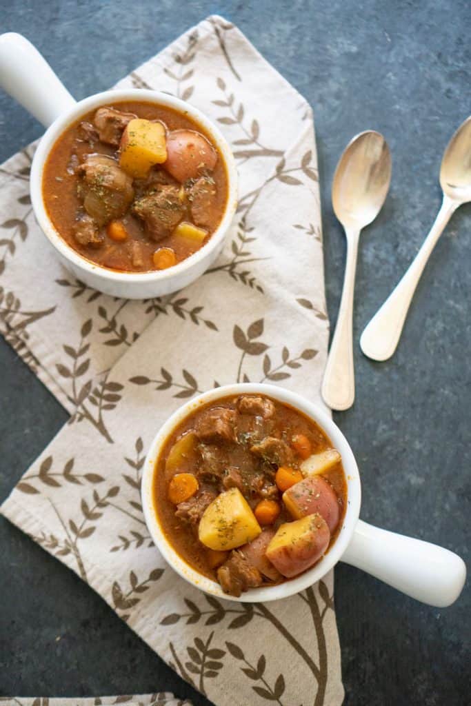 overhead view of two white bowls instant pot beef stew  with brown patterned napkin and two spoons