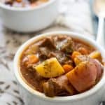close up of instant pot beef stew in white bowl with brown patterned napkin
