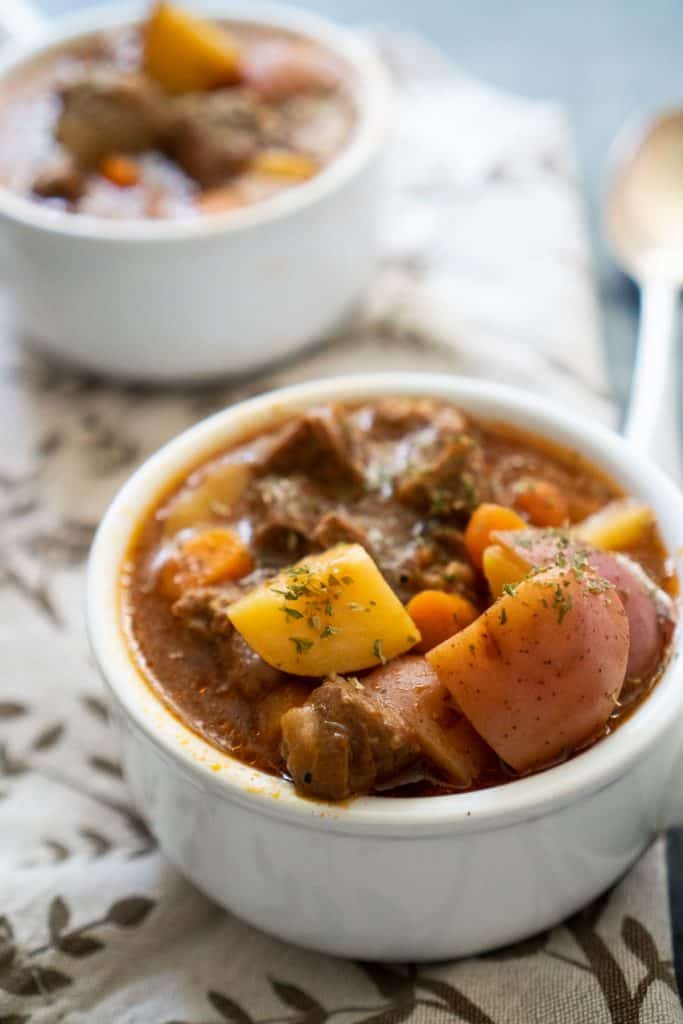 close up of instant pot beef stew in white bowl with brown patterned napkin