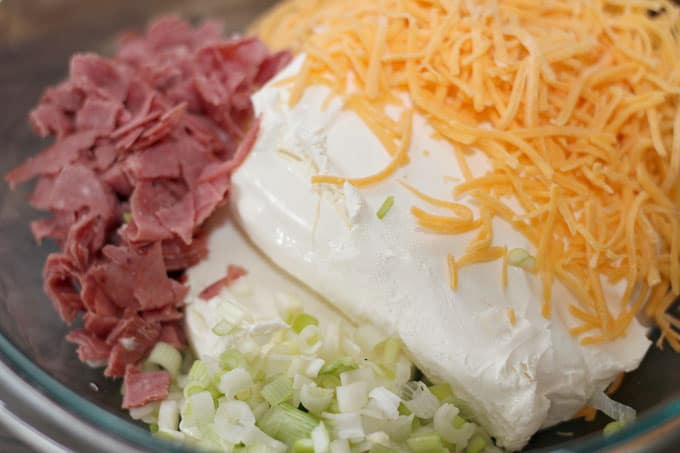 bacon bits, shredded cheddar cheese, cream cheese, and diced onions in glass bowl