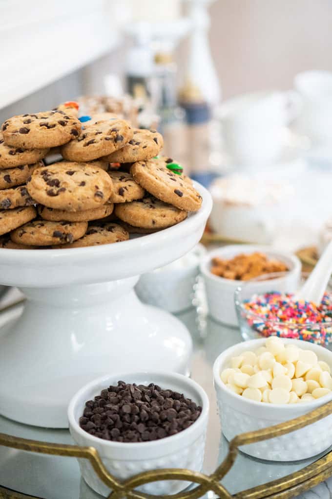 cookies on white cake stand surrounded by hot chocolate toppings in small bowls below