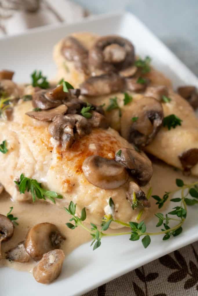  Two pieces chicken marsala with mushrooms, herb sauce, and fresh parsley on white plate