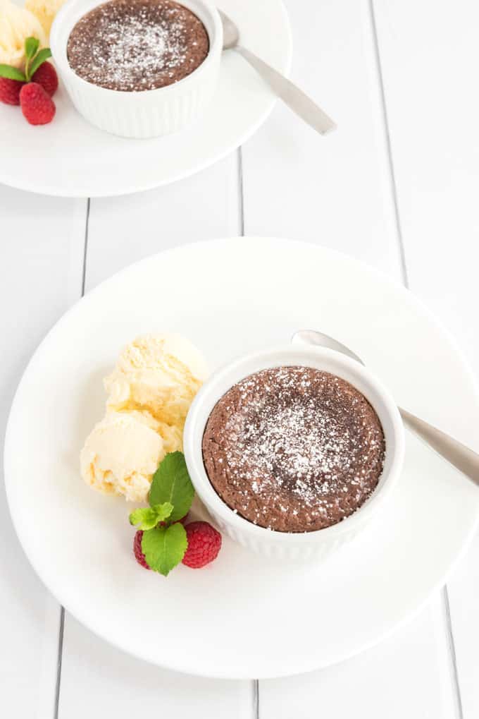 two ramekins of chocolate melting cake on white saucers with vanilla ice cream raspberries mint