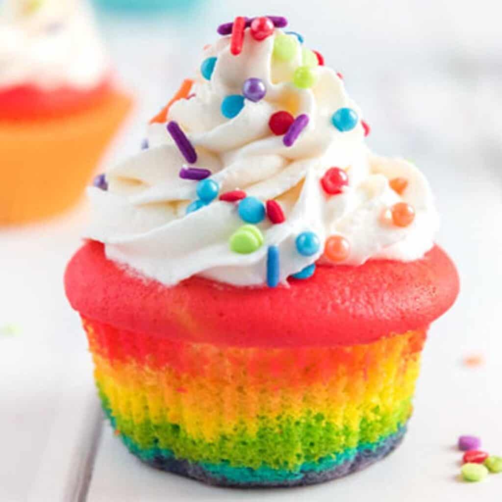 close up of rainbow cupcake with cream cheese frosting and rainbow sprinkles