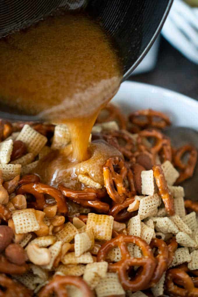 pouring toffee mixture over snack mix with pretzels chex cereal nuts