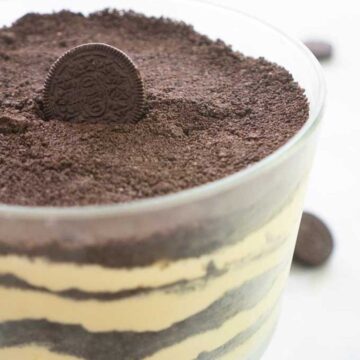 oreo dirt cake layered in a glass trifle dish topped with whole oreo cookie