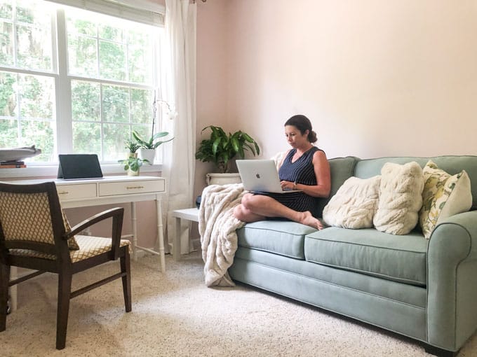 girl with laptop sitting on blue loveseat with desk and window