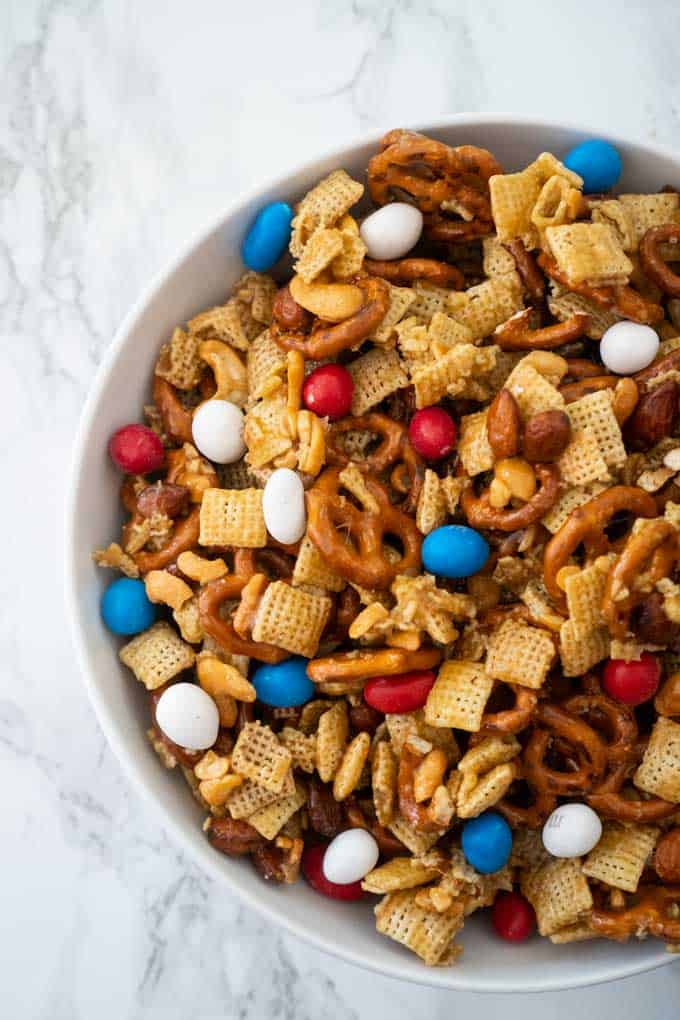 overhead view of sweet and salty snack mix in white bowl with marble background