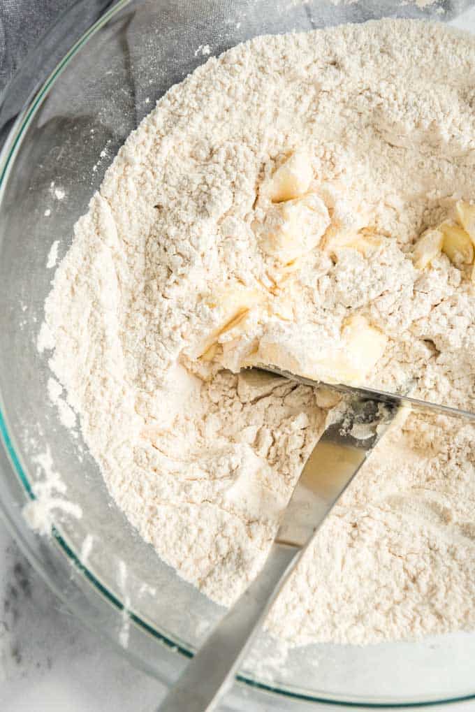 two knives cutting butter into flourin a glass bowl