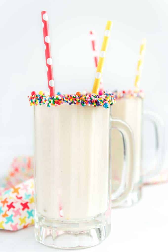 cake batter healthy smoothie in glass with sprinkles on rim and colorful straw