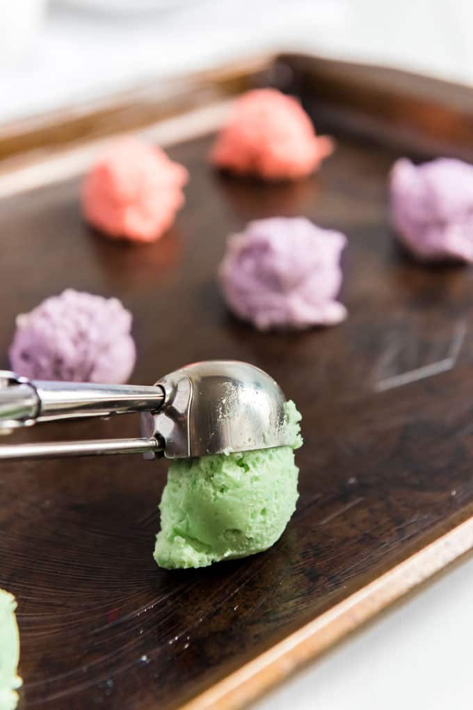 scooping colorful cookie dough pink purple green onto baking sheet