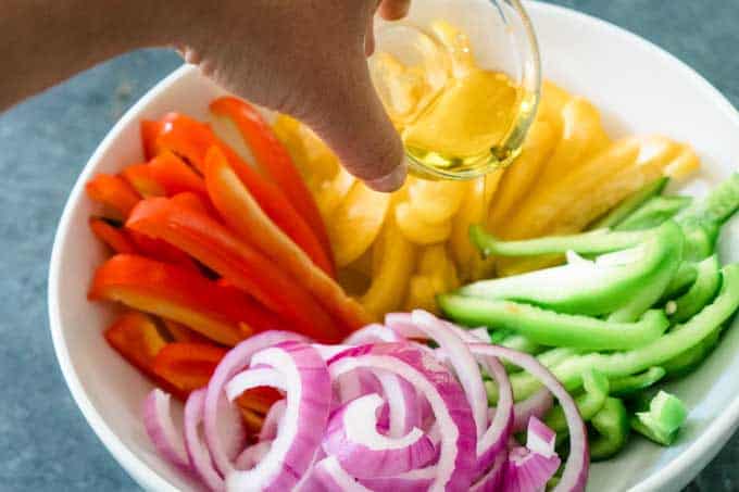 pouring olive oil over chopped bell peppers and red onion