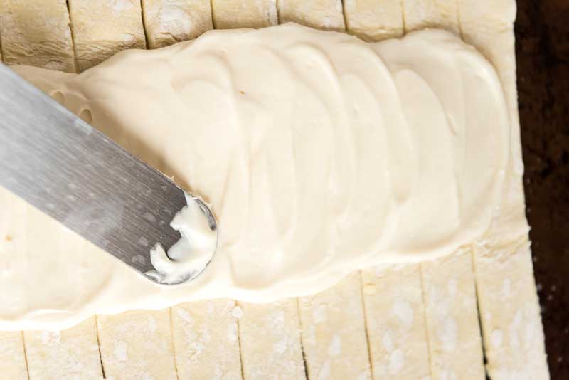 spreading cream cheese on puff pastry to make danish