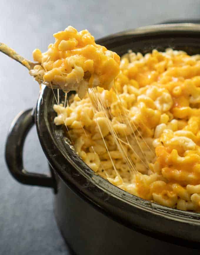 scooping crock pot mac and cheese out of slow cooker