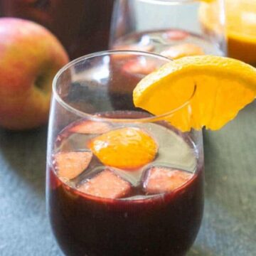 red wine sangria with cut apples and oranges in stemless wine glass