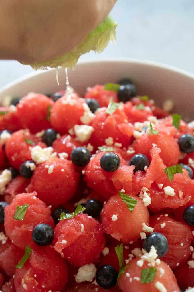 hand squeezing lime over watermelon salad with feta blueberries mint