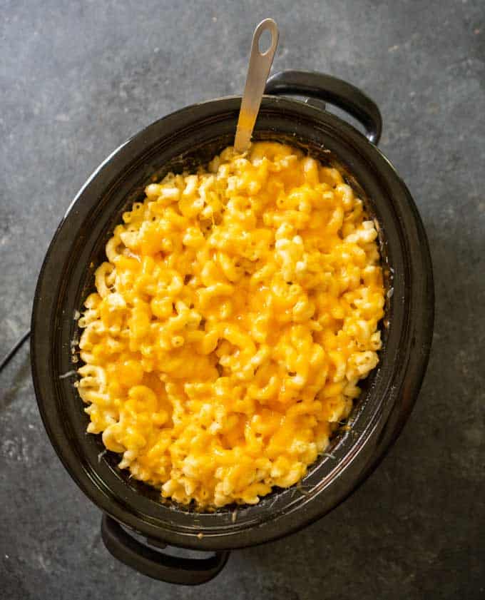 overhead view of slow cooker mac and cheese in a black crock pot with spoon sticking out