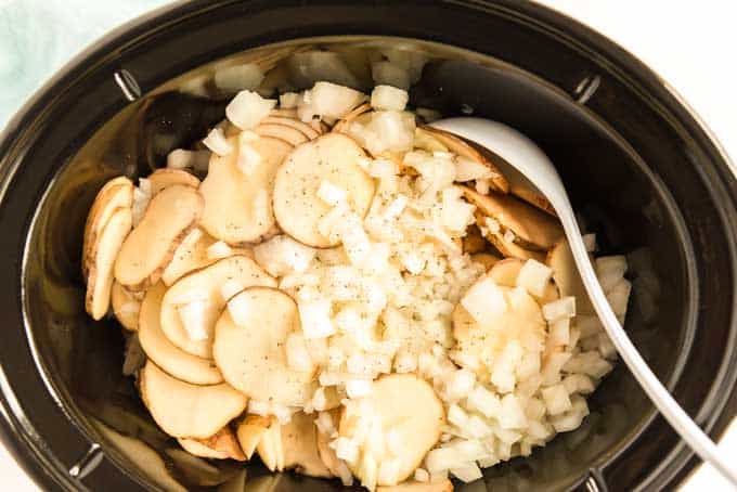 slow cooker with thinly sliced potatoes and diced onion