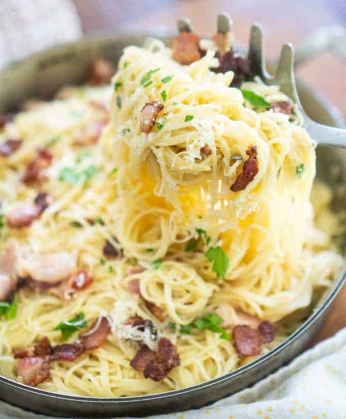 scooping up pasta carbonara with bacon from large skillet