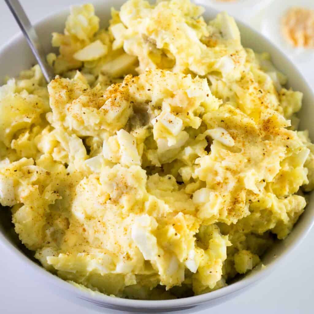 deviled egg potato salad in white bowl with spoon
