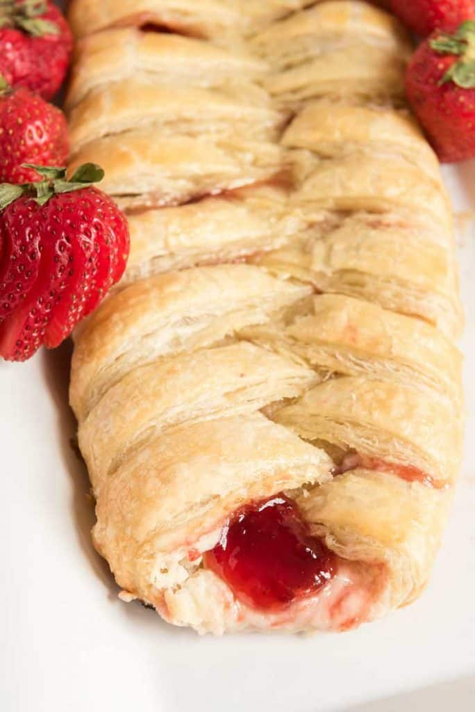 braided strawberry cream cheese danish on white plate with strawberries