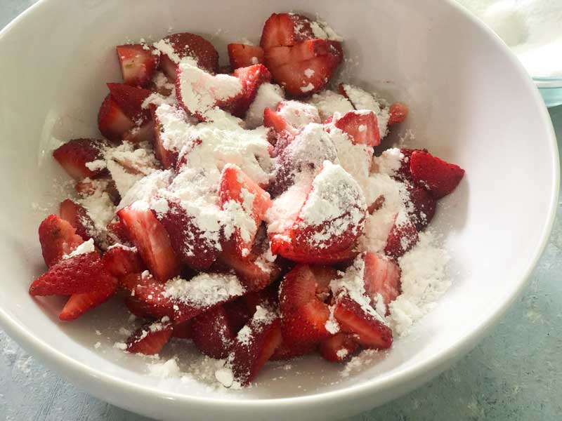 cut strawberries in white bowl with sugar