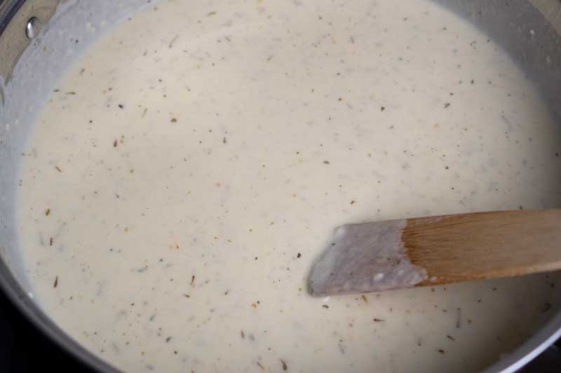 stirring homemade alfredo sauce in skillet with wooden spoon