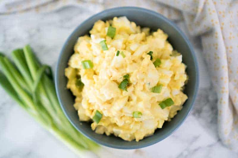 egg salad in a gray bowl with chopped green onion on top 